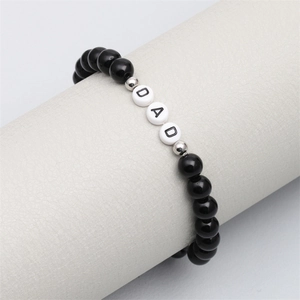 Close-up of DAD letter beads on black beaded bracelet displayed on a white leather stand