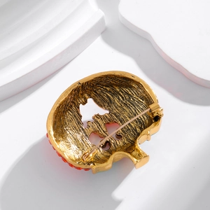 Golden skull brooch with red gemstones and textured back in professional studio lighting