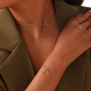 Minimalist silver bow necklace and bracelet set shown on model in olive suit