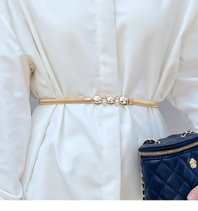 Close-up of golden elastic metal waist belt with rhinestone buckle on white clothing