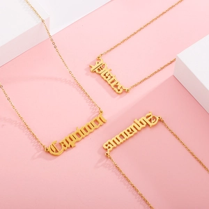 Close-up of 18k gold zodiac name necklaces with Gothic font on pink background