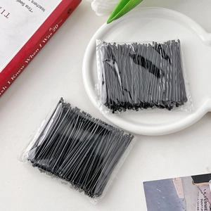 Macro detail of bulk black wavy metal hairpins in clear packaging on a white plate