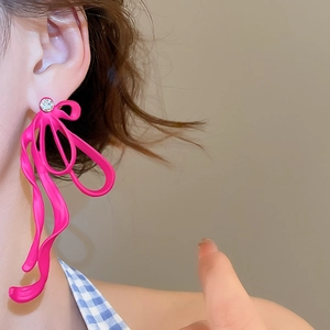 Close-up of rose pink ribbon earrings with rhinestone detail on a female model