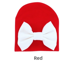 Detailed view of red infant beanie featuring a large white decorative bow on soft knit fabric