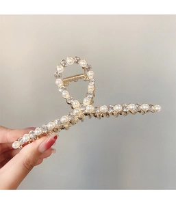 Détail d'une pince à cheveux dorée ornée de perles blanches et de strass brillants