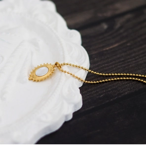Macro shot of sunburst shell pendant on a gold bead chain over white texture