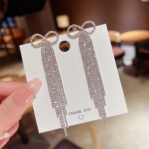 Close-up of sparkling rhinestone bow tassel earrings on a display card