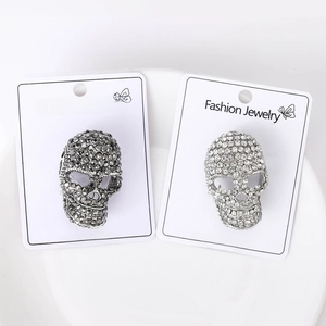 Close-up of black and silver skull brooches with shimmering rhinestones on white card