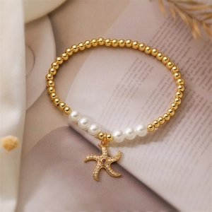 Détail du bracelet en perles dorées avec breloque étoile de mer et pierre rouge