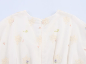 Détail de la broderie florale et de la fermeture éclair invisible sur la robe crème