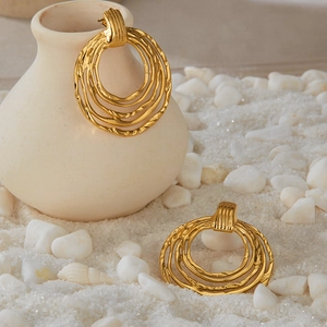 Macro shot of layered gold hoop earrings with metallic texture on white sand background
