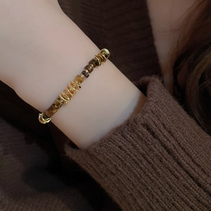 Detail of geometric bracelet featuring tiger eye stones and golden beads on wrist