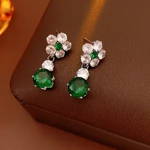 Elegant emerald green flower drop earrings with zircon crystals on a dark leather texture
