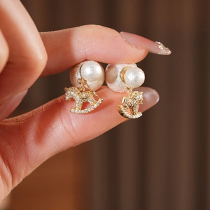 Close-up of gold rocking horse earrings with micro-set crystals and white cotton pearl
