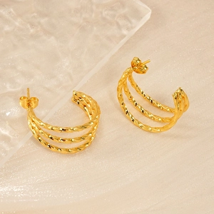 Close-up of golden 18K twisted hoop earrings on beige textured fabric background