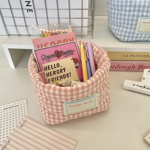 Detail of pink plaid quilted storage basket with pens and stationery on a desk