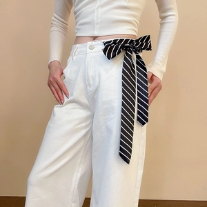 Detail of high-waist white wide-leg trousers with a black and white striped bow tie belt