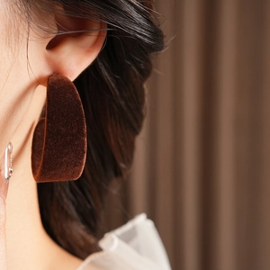 Close-up of a model wearing brown velvet C-shaped hoop earrings with a leopard texture