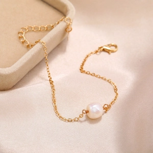 Detailed close-up of a gold-plated bracelet featuring a white pearl on silk background