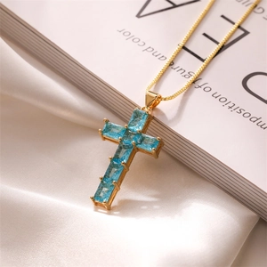 Detailed close-up of a golden cross necklace with light blue stones on white silk fabric