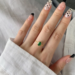 Detail of gold chain ring featuring an oval green zircon stone worn on a hand