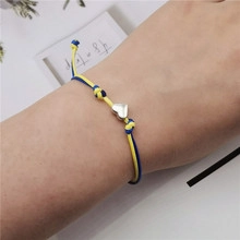 Detail of yellow and blue woven rope bracelet with a heart-shaped silver pendant on wrist