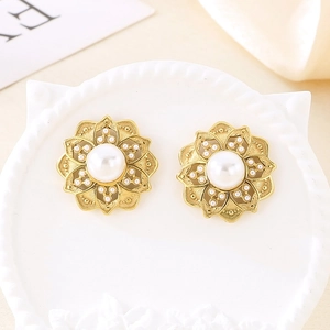 Macro detail of gold flower earrings with central pearl on an embossed white plate