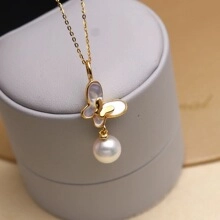 Detailed macro shot of golden butterfly necklace with white shell wings and a hanging pearl