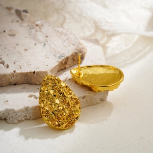 Detailed macro view of gold water drop stud earrings with textured metallic surface