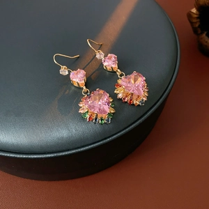 Detailed close-up of gold heart earrings with pink stone and colorful crystals on a black stand