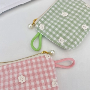 Close-up of floral embroidery on plaid cosmetic bag with pearl zipper pull detail
