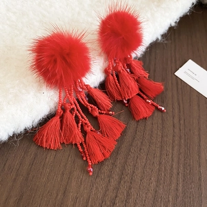 Detail view of red pompom earrings with beaded charms and long cotton fringe tassels