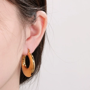 Close-up of chunky gold-plated U-shaped earrings on model showing glossy metallic texture