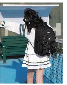 Student backpack in black nylon with heart charm shown against outdoor tennis court backdrop