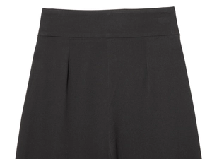 Detail of high waisted black trousers showing precise pleats and smooth woven fabric texture