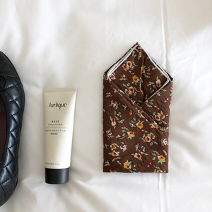 Flat lay of brown floral cotton linen handkerchief next to rose hand cream and shoes