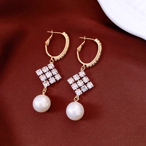 Vue macro de boucles d'oreilles losanges plaquées or 18k avec perles sur du satin