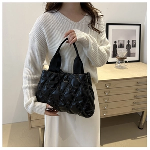 Quilted black tote bag with diamond stitching shown on a model in a cozy indoor setting