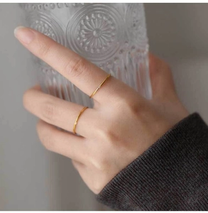 Close-up of two minimalist gold thin rings with tiny crystals on a model holding glass