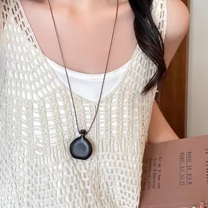 Ethnic minimalist resin stone pendant necklace with brown cord on a white knit vest