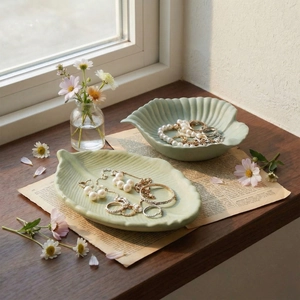 Leaf and shell shaped ceramic jewelry trays in pale green on a rustic wooden windowsill
