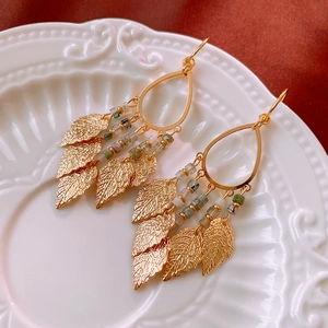 Detail of vintage gold leaf tassel earrings with green beads on a white relief plate