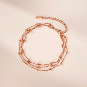 Detail of rose gold multi-layer beaded anklet with S.STEEL stamp on a soft pink background