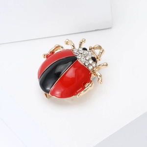 Red and black enamel ladybug brooch with gold trim and rhinestones on a white podium