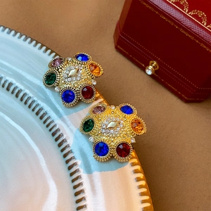 Gold-plated floral stud earrings featuring colorful rhinestones on a ceramic dish