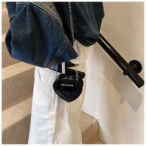 Mini heart-shaped crossbody bag in black patent leather with chain strap on a model