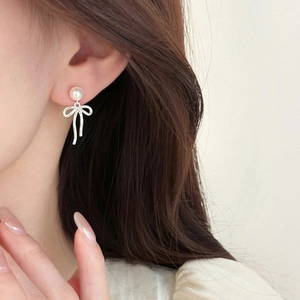 Close-up of model wearing bow pearl drop earrings with silver finish and soft lighting