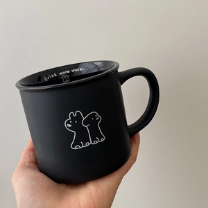 Close-up of black ceramic mug with 'drink more water' text and hand-drawn dog graphic