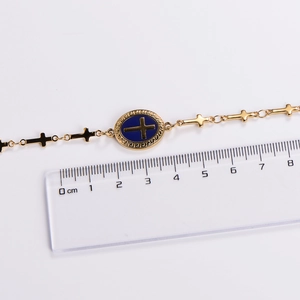 Detailed view of golden cross bracelet with blue center charm showing dimensions on a ruler