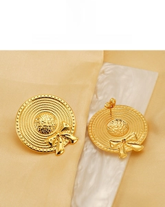 Détail de boucles d'oreilles chapeau à nœud plaquées or 18K sur marbre chic